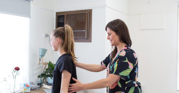 Female osteopath assessing a teen with hands on back
